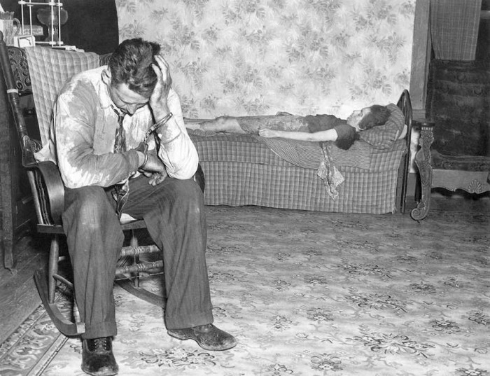 Fotogrāfija publicēta 1943. gada 26. aprīlī ar parakstu: “Dziļā nožēlā, ieslēgts roku dzelžos, Līrojs Laskombs , 32, sēž istabā, kurā atrodas viņa mirusī sieva… Ņujorkas policija sacīja, ka viņš to nogalinājis ar medību bisi, kad viņa pametusi viņu ar trim bērniem, tādēļ, ka viņš interesējies par citu sievieti. Laskombam izvirzīta apsūdzība pirmās pakāpes slepkavībā.” Piezīmēs par fotogrāfiju var arī izlasīt, ka slepkavība izdarīta sievietes vecāku mājā pēc tam, kad viņa bija atteikusies atgriezties pie vīra. Viņš iešāva sievai kaklā, uz vietas viņu nogalinot. Arestēts Laskombs apgalvoja, ka gribējis sievai tikai piedraudēt un nav zinājis, ka ierocis ir pielādēts. Šo apgalvojumu atspēkoja Laskomba dēls, kurš policijā pateica, ka slepkavības dienā redzējis tēvu pielādējam bisi. (Foto: Daily News)